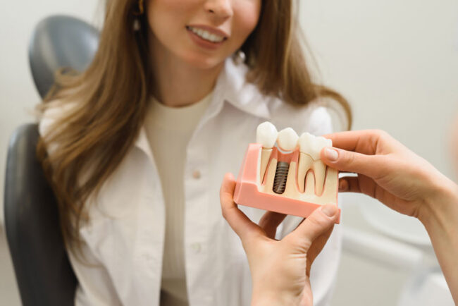 dental-patient-getting-shown-an-implant-model Dental Patient Getting Shown A Dental Implant Model During Her Consultation in Westminster, CO
