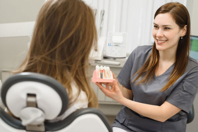 dental-assistant-showing-off-dental-implant-model a dental assistant showing a patient a dental implant model