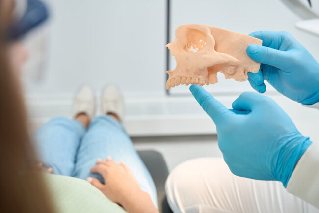 dentist-pointing-at-a-jawbone-model-to-a-dental-patient Dentist pointing at a jawbone model to a dental patient.