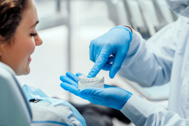 adentist-showing-an-implant-patient-a-dental-implant-model a dentist showing an implant patient a dental implant model.